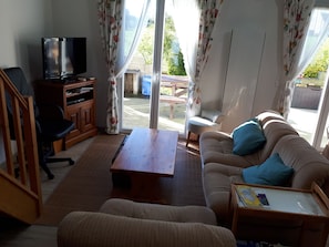 A living room with a sofa, a coffee table, a TV, and a sliding glass door leading to an outdoor area.