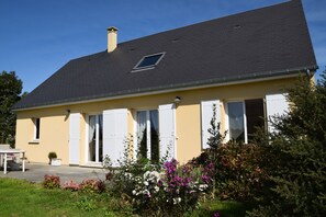 A two-story house with a dark roof, white shutters, and a small window.