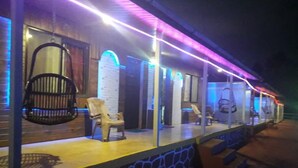 Un espace extérieur abrité, avec des chaises et des tables, un mur en pierre et un plancher en bois.