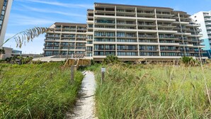 Ein mehrstöckiges Hotel mit modernem Design, das Balkone auf jeder Etage und einen Weg zum Eingang bietet.