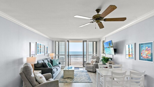 Ein geräumiges Wohnzimmer mit Balkon, Deckenventilator und Essbereich mit weißen Stühlen.