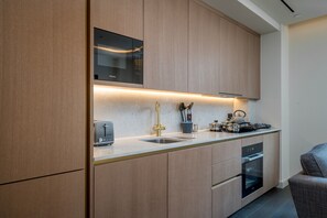 A modern kitchen with wooden cabinets, a built-in microwave, a sink, and an oven. - Luxury Residence - TCRW Soho Square (London)