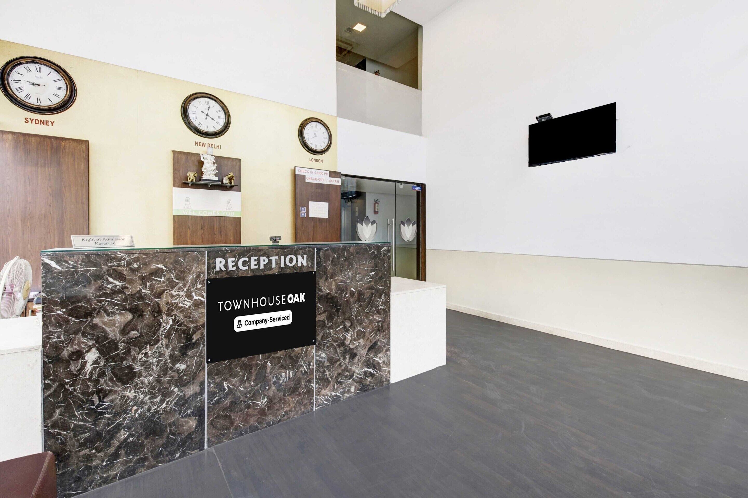 A reception desk with clocks indicating Sydney, New Delhi, and London times, a reception sign, and a refrigerator.