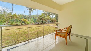 A balcony with a wooden chair, a metal railing, and a view of a garden with palm trees. - Deluxe Thiruvallam Lakeview (Thiruvananthapuram)