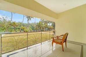 A balcony with a wooden chair, a metal railing, and a view of a garden with palm trees.