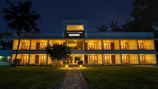 A two-story building with a sign reading 'TOWNHOUSE OAK' and 'Company-Serviced.' - Deluxe Thiruvallam Lakeview (Thiruvananthapuram)
