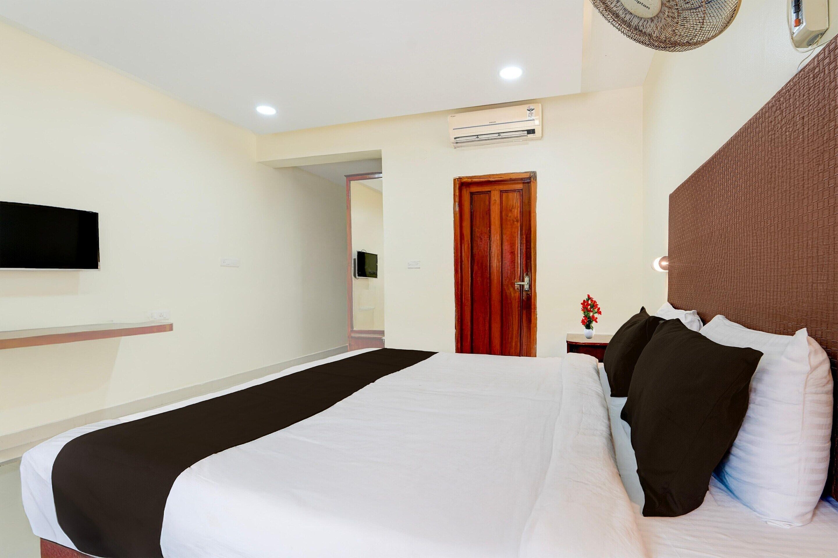 Una habitación de hotel con una cama, un televisor de pantalla plana montado en la pared, un equipo de aire acondicionado y una puerta de madera.