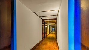 Un long couloir étroit, typique d’un hôtel, avec un plancher en bois et des murs blancs.
