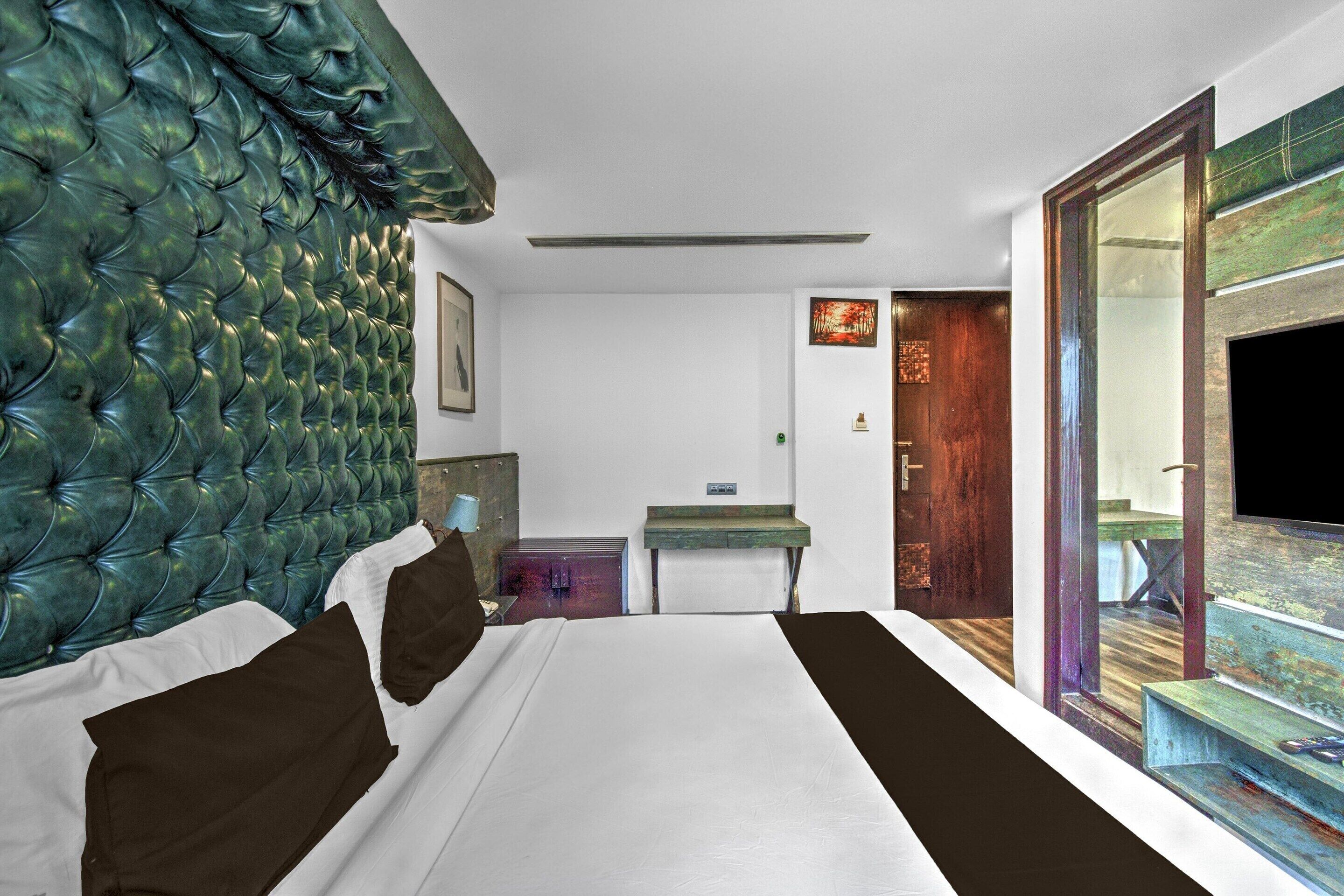 A hotel room with a tufted headboard, a bed with white and brown bedding, a desk, and a view through a glass door.