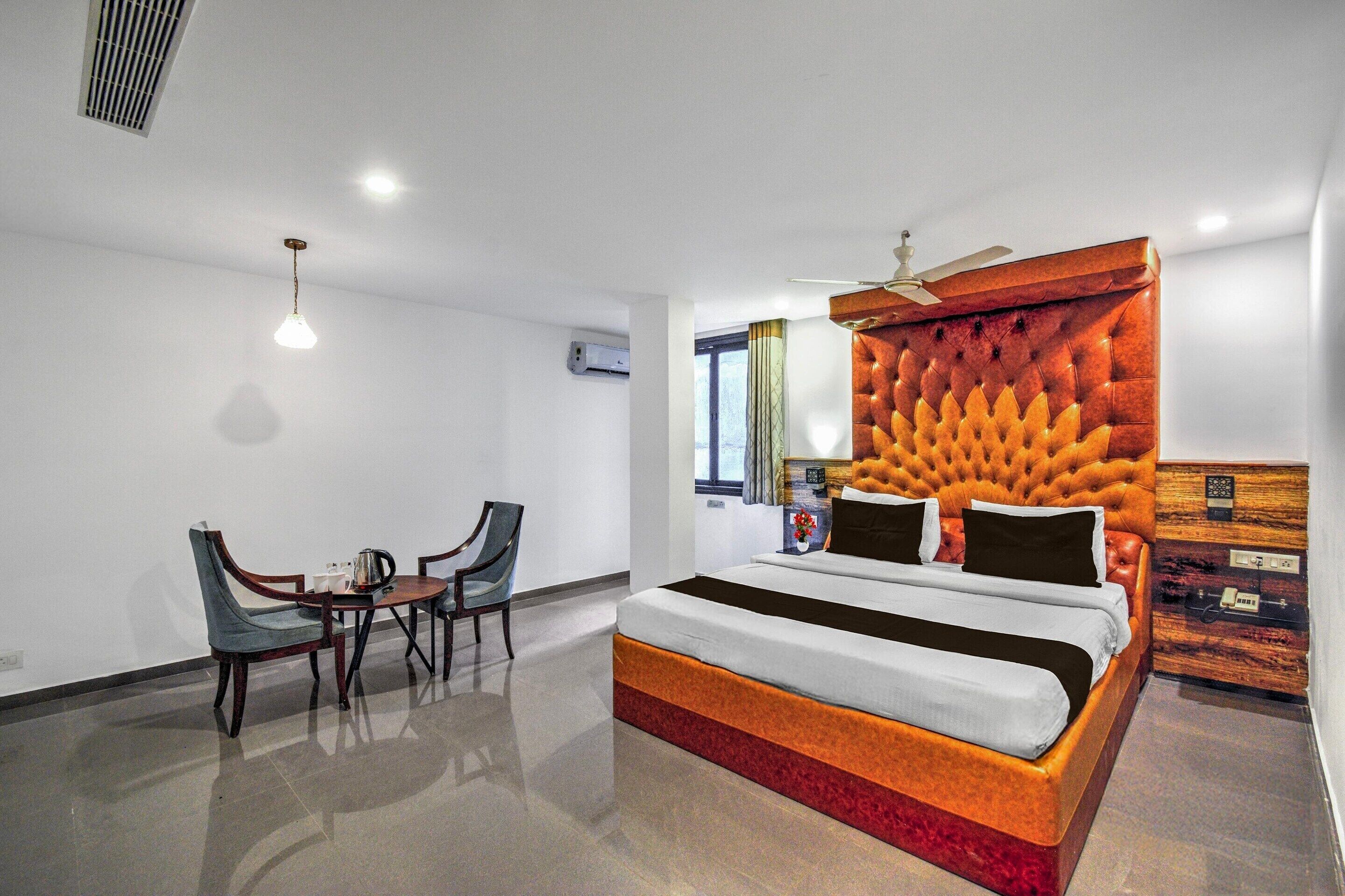 Ein modernes Hotelzimmer mit einem großen Bett, einem Schreibtisch mit Stühlen, einem Deckenventilator und einem Fenster mit Vorhängen.