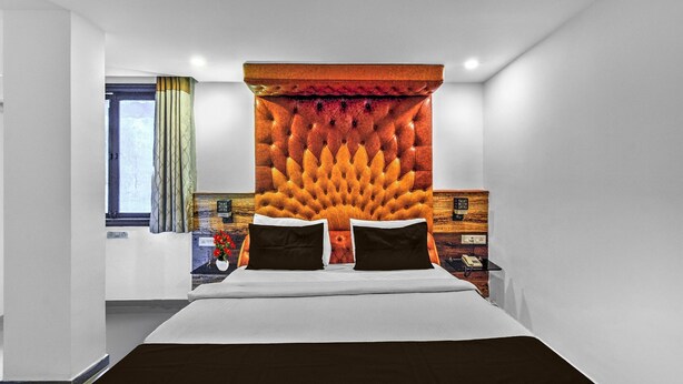Une chambre d’hôtel moderne avec un grand lit, une tête de lit capitonnée, une table de chevet avec une lampe et une fenêtre avec des rideaux.