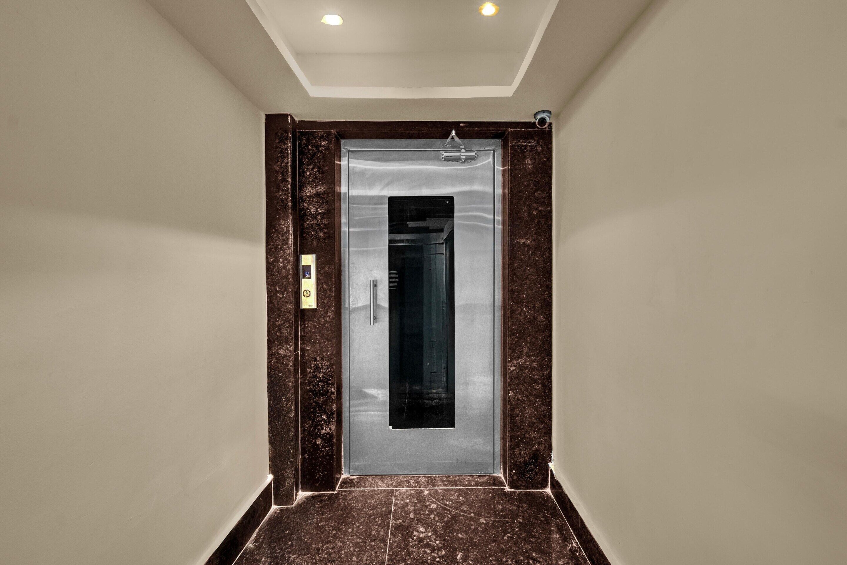Een moderne lift met een metalen afwerking, een bedieningspaneel aan de linkerkant en een marmeren vloer.
