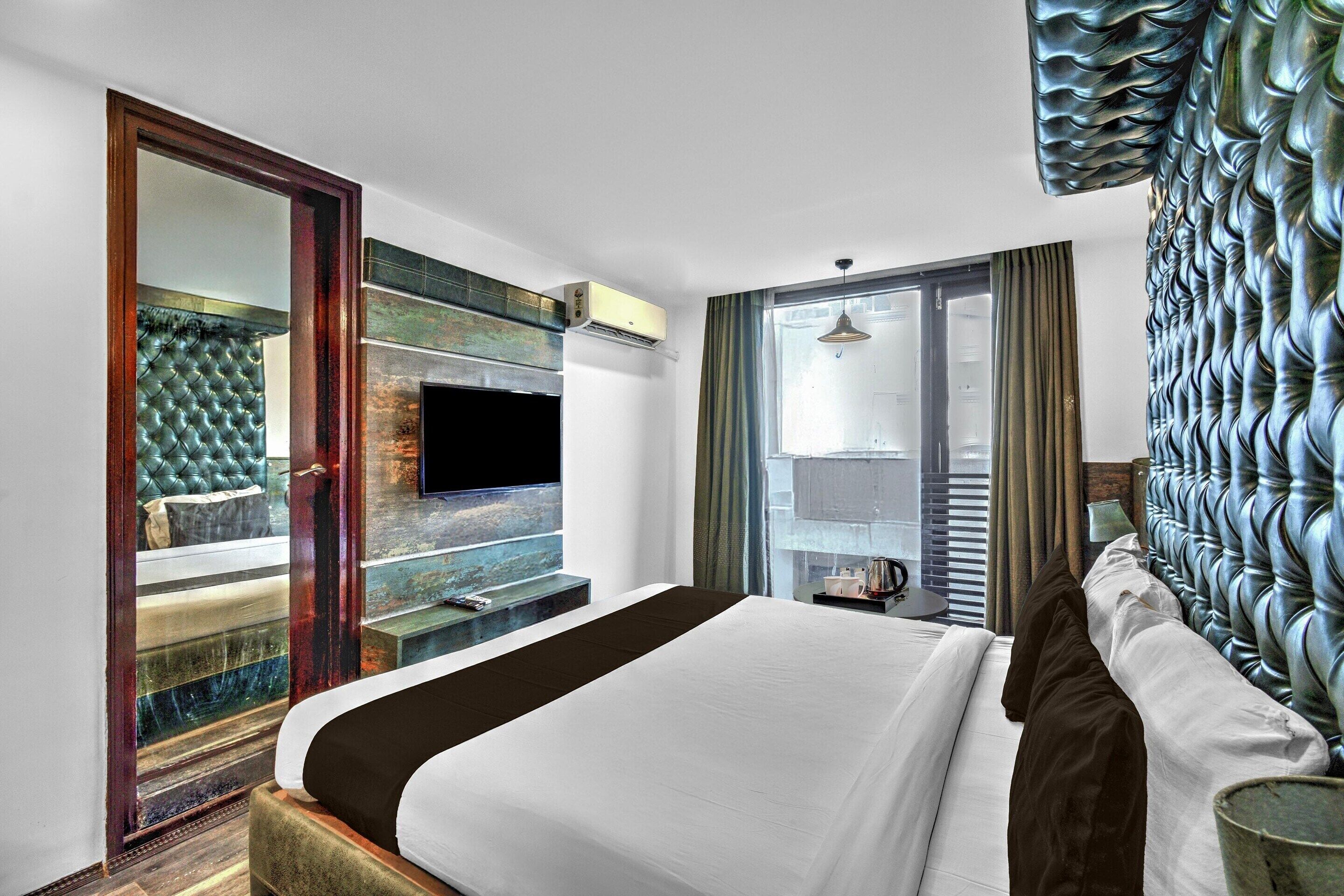 A hotel room with a bed, a television mounted on the wall, a window with curtains, and a decorative wall panel.