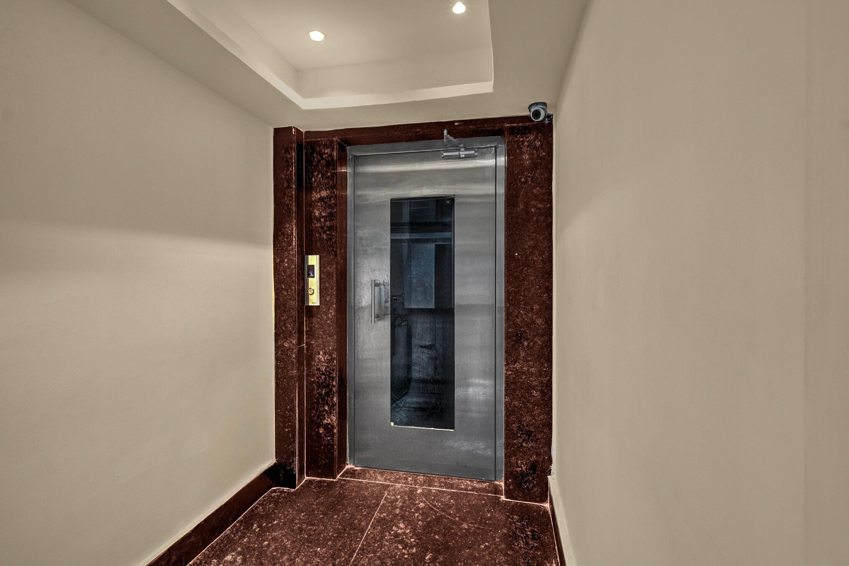 A modern elevator with a metallic finish, a marble floor, and a wall-mounted control panel.
