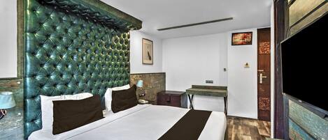 Habitación de hotel con una cama grande, cabecero de madera, mesita de noche con lámpara, escritorio con silla y televisor.