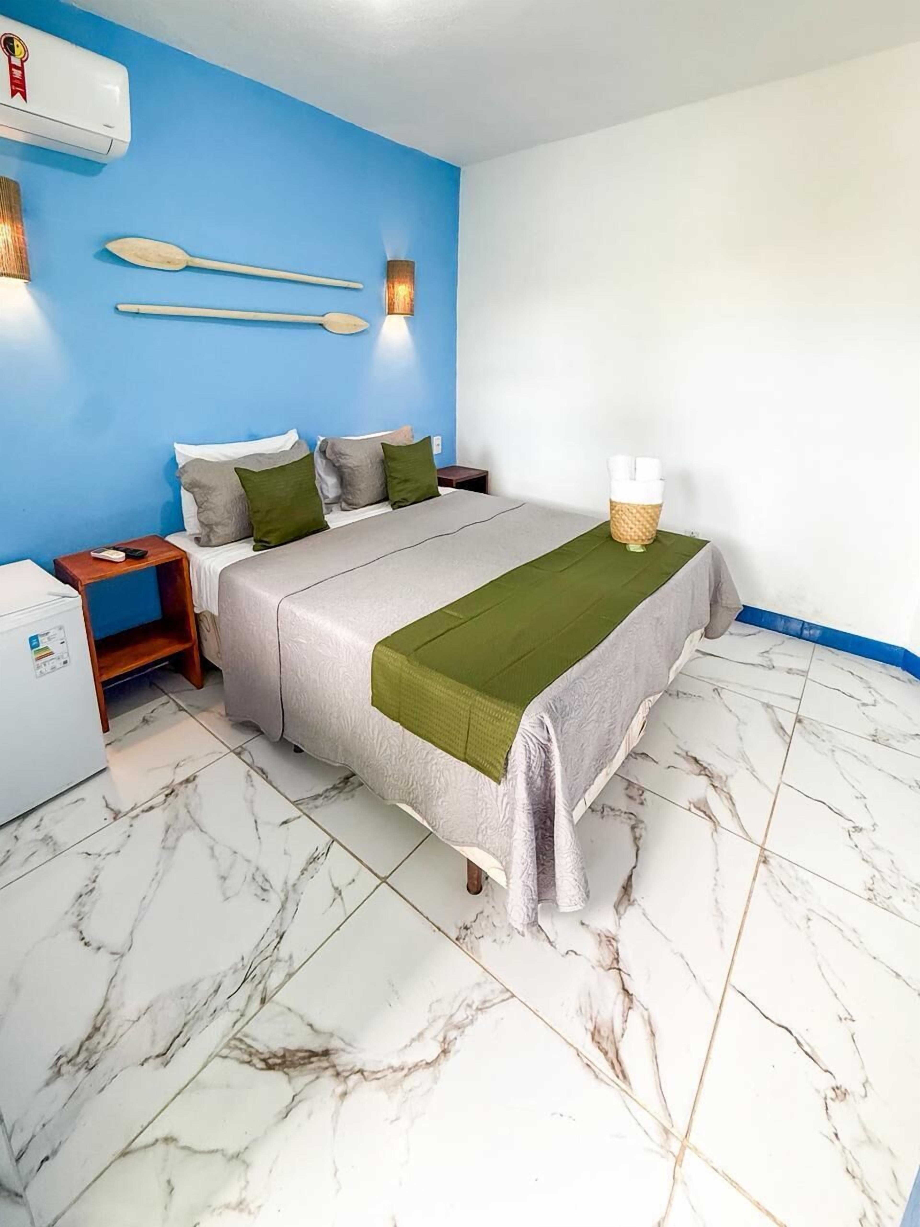 A hotel room with a bed, a nightstand, a wall-mounted heater, and a white refrigerator.
