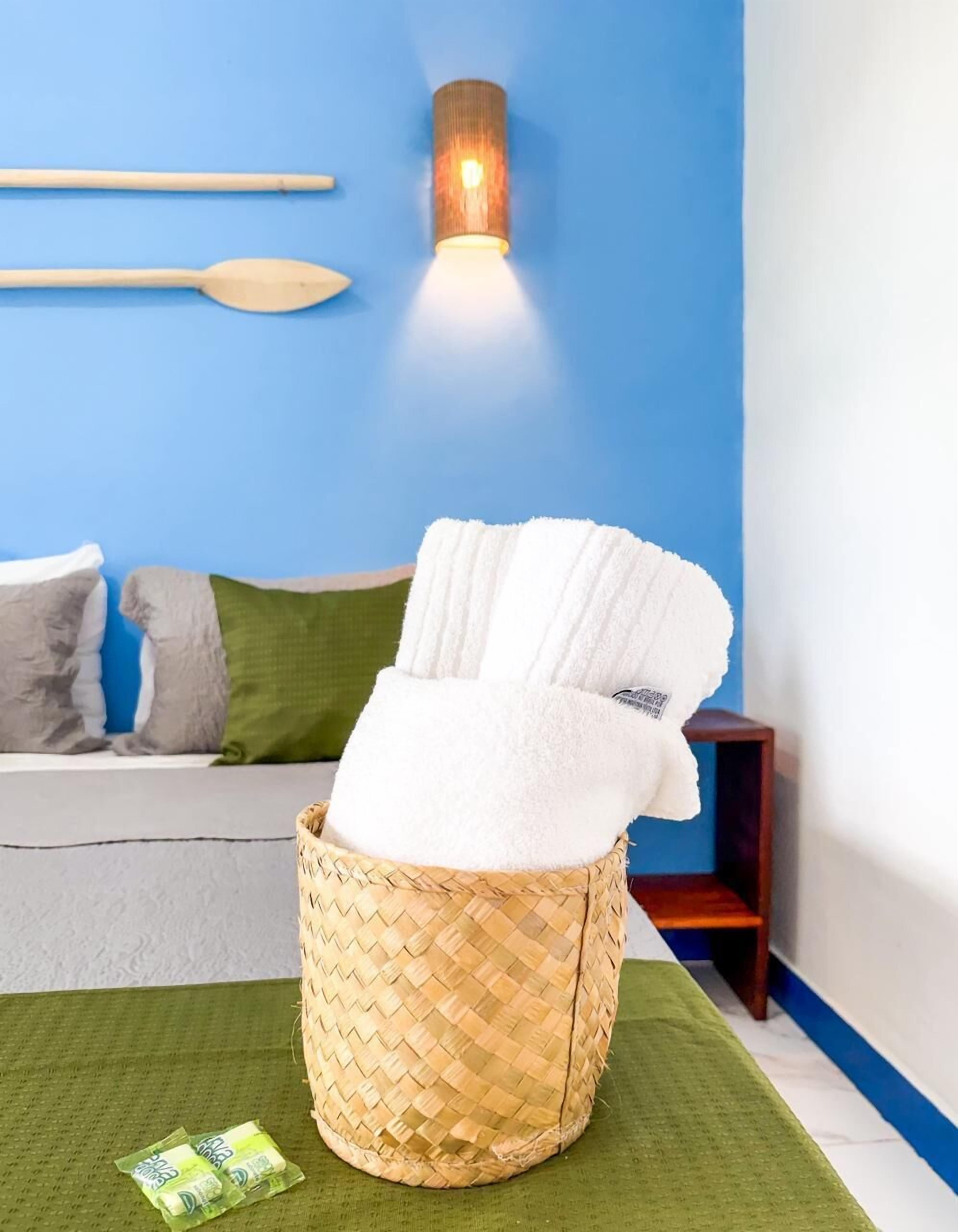 A room with a woven basket containing a white towel, a wooden spoon on the wall, and a small wooden side table.