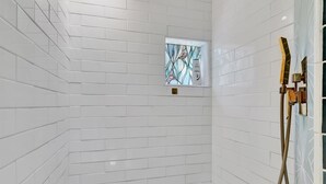 A shower with white tiled walls, a mosaic floor, and a small window with stained glass. - Gulfport Studio Near John s Pass the Beach (Gulfport)
