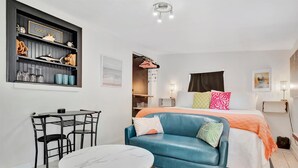 A bedroom with a bed, a blue sofa, a small table, a desk, and a shelf with various items. - Gulfport Studio Near John s Pass the Beach (Gulfport)