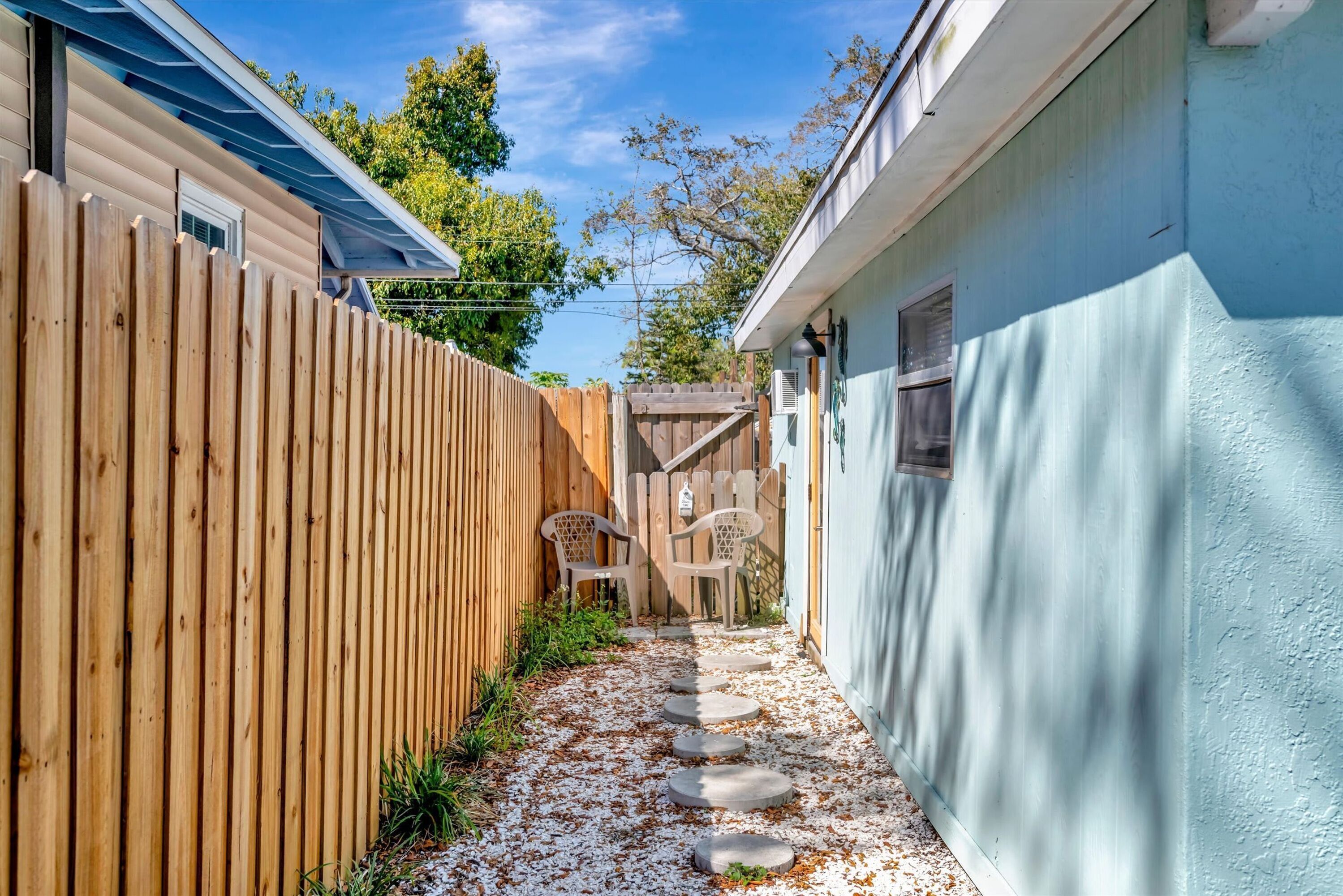 Un sentier étroit, parsemé de pierres plates, mène à une clôture en bois et à un bâtiment bleu.