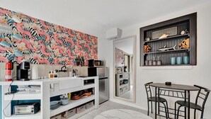 A modern kitchen with a white countertop, a dining table with chairs, a patterned wall, and a shelf with decorative items. - Gulfport Studio Near John s Pass the Beach (Gulfport)