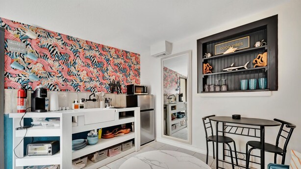 A modern kitchen with white cabinetry, a microwave, and a stainless steel refrigerator. There is a dining area with a round table and two chairs. - Gulfport Studio Near John s Pass the Beach (Gulfport)