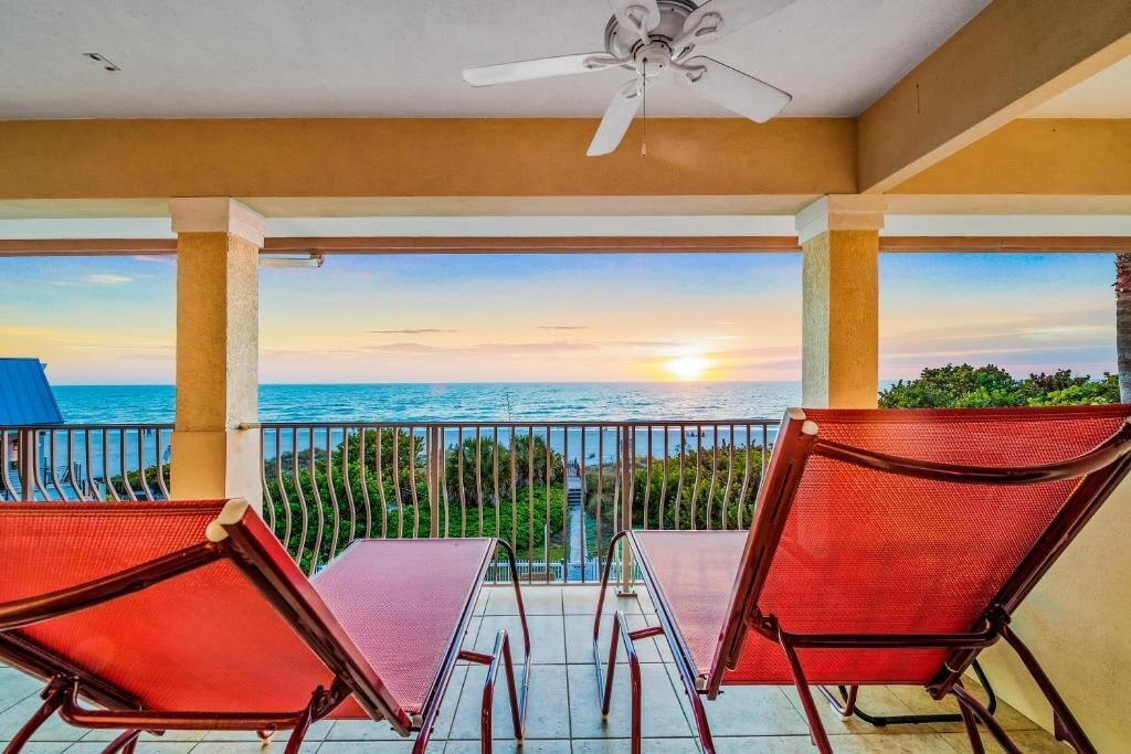 A balcony with two chairs and a table, overlooking a sunset over the sea.