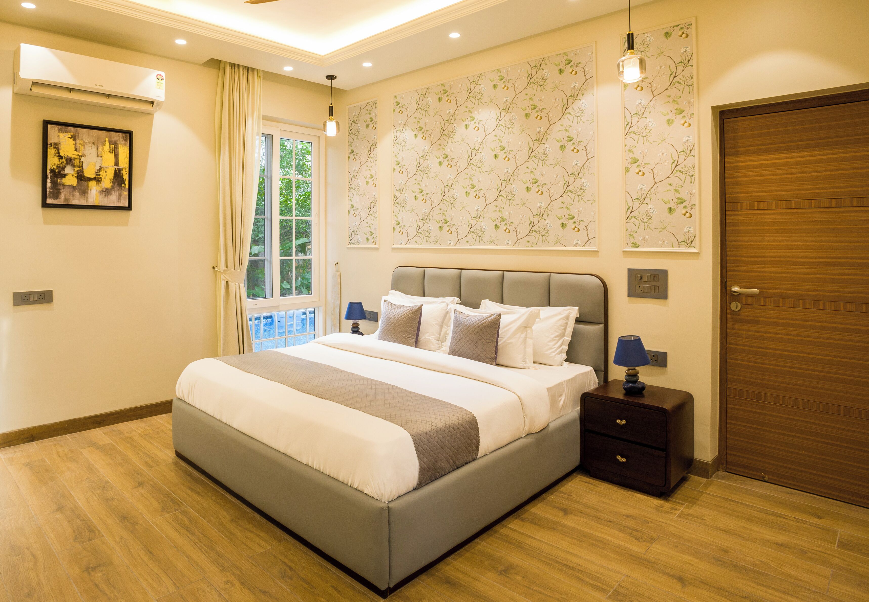 A modern bedroom with a large bed, bedside lamps, a nightstand, a wooden door, and a window with curtains.