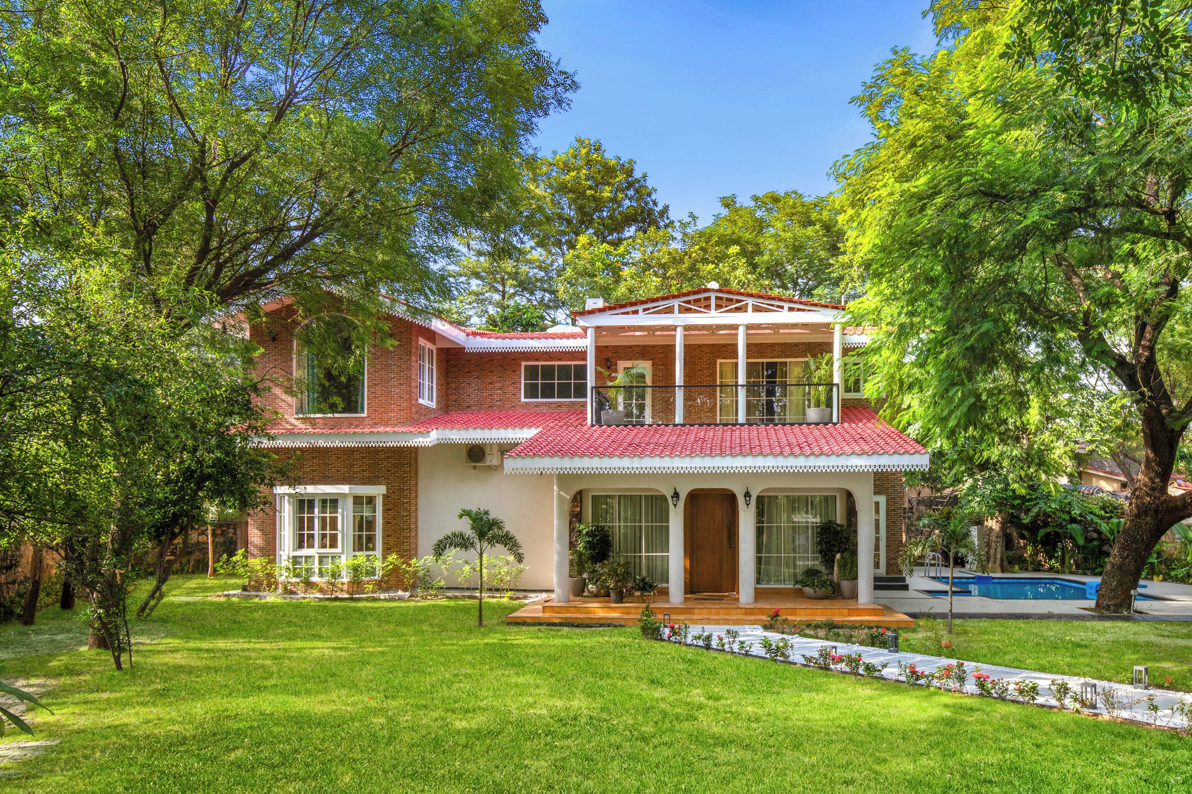 A two-story house with a red-tiled roof, a covered porch, and a swimming pool in the background.