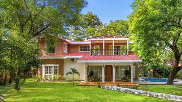 A two-story house with a red-tiled roof, a covered porch, and a swimming pool in the background.