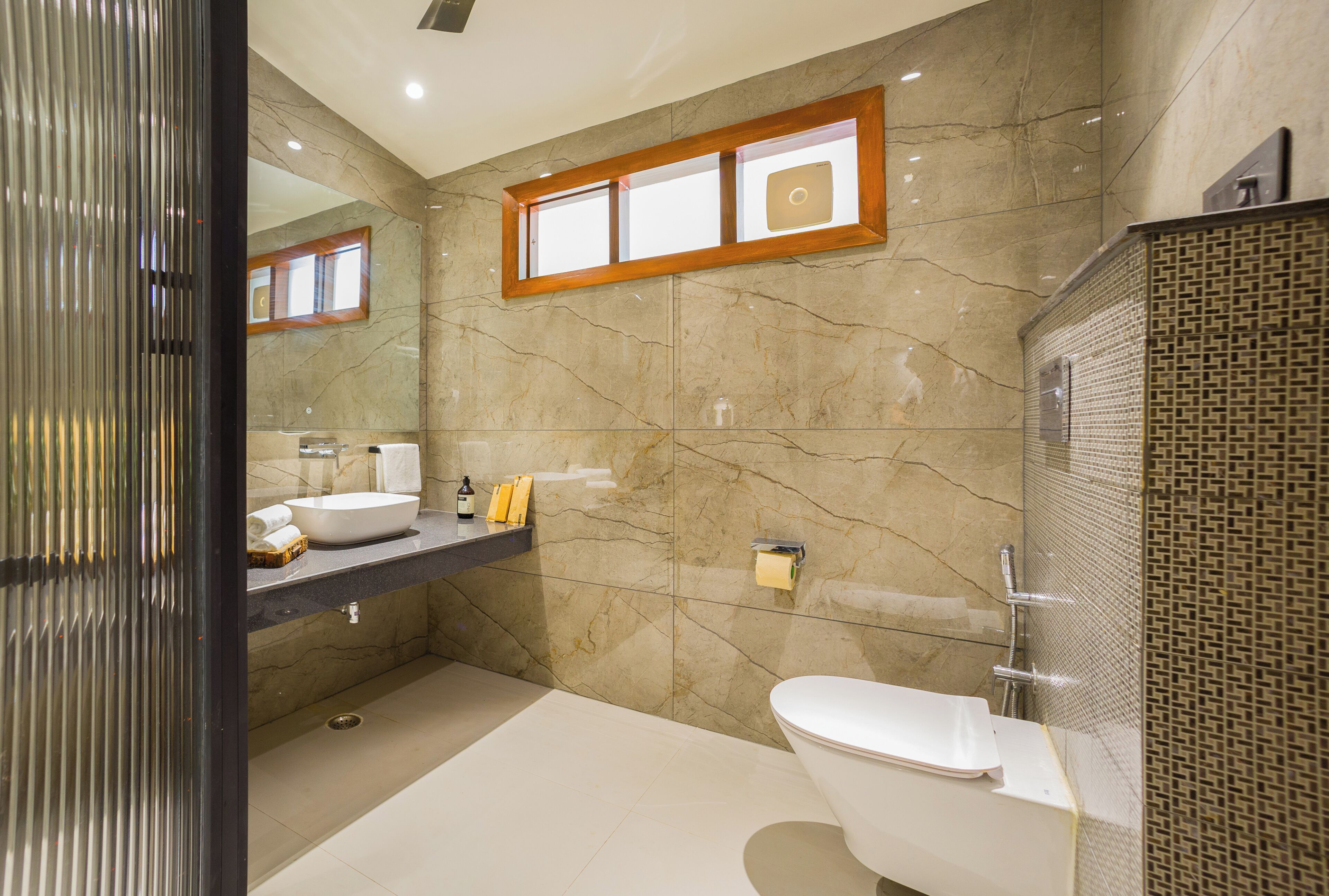Une salle de bain moderne avec un mur en marbre, un lavabo encastré, des toilettes et un espace douche.