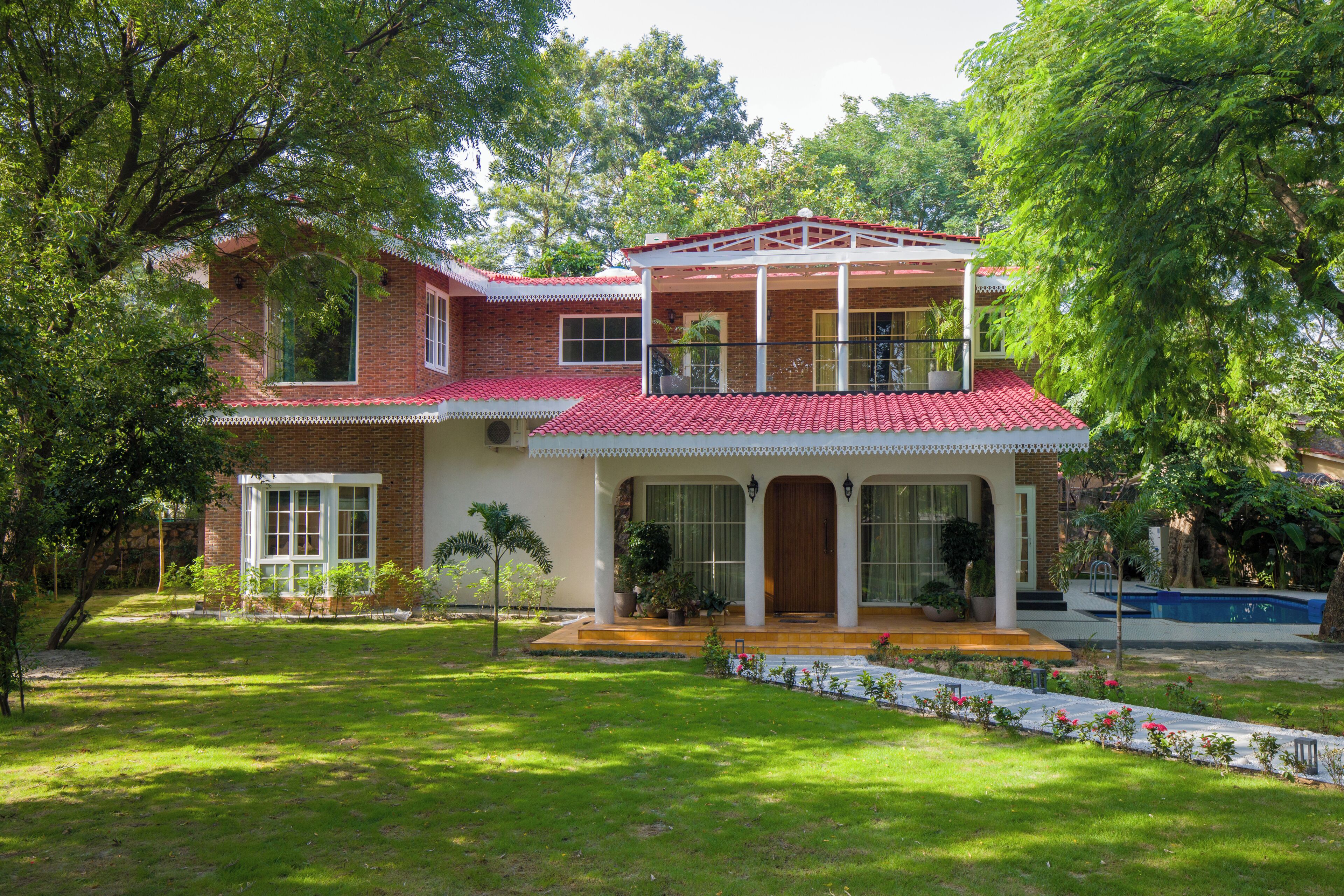 A two-story house with a red-tiled roof, a balcony, and a well-maintained garden.