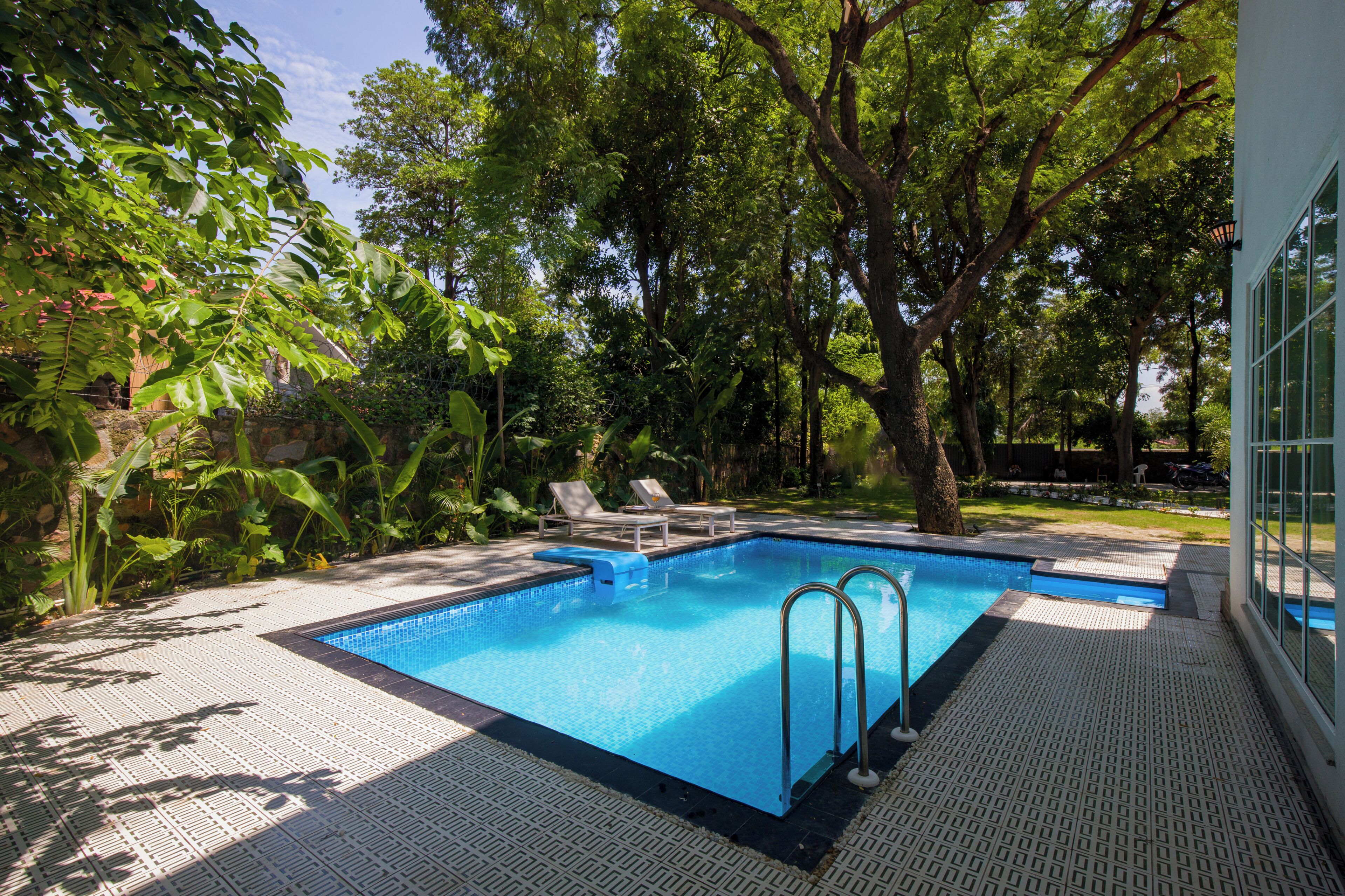 A swimming pool with two ladders, surrounded by trees and a covered patio area.