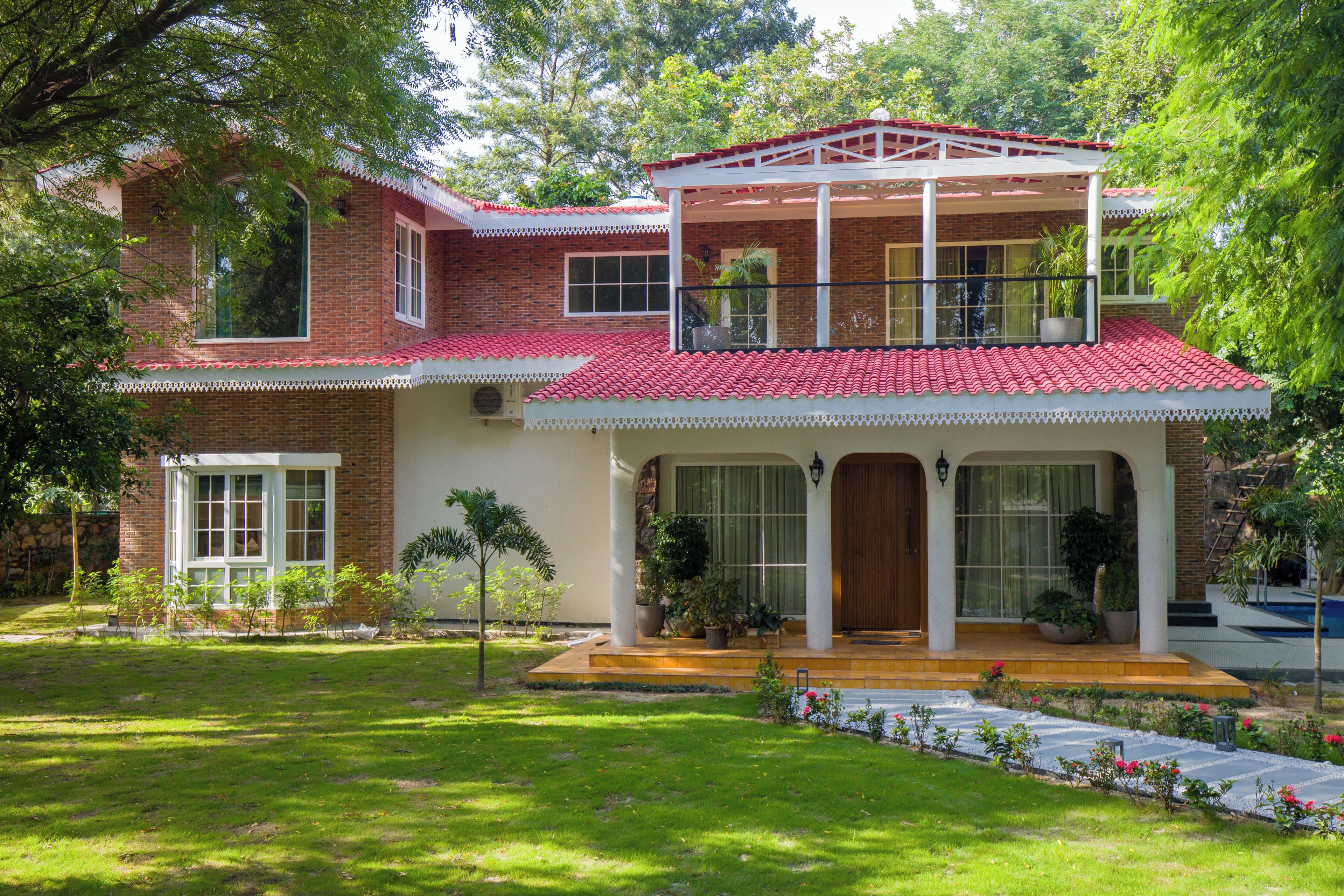 Une maison à deux étages, avec un toit recouvert de tuiles rouges, un balcon et un jardin bien entretenu.
