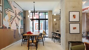 Ein moderner Essbereich mit Tischen, Stühlen, Wandgemälde und einem großen Fenster mit Vorhängen.