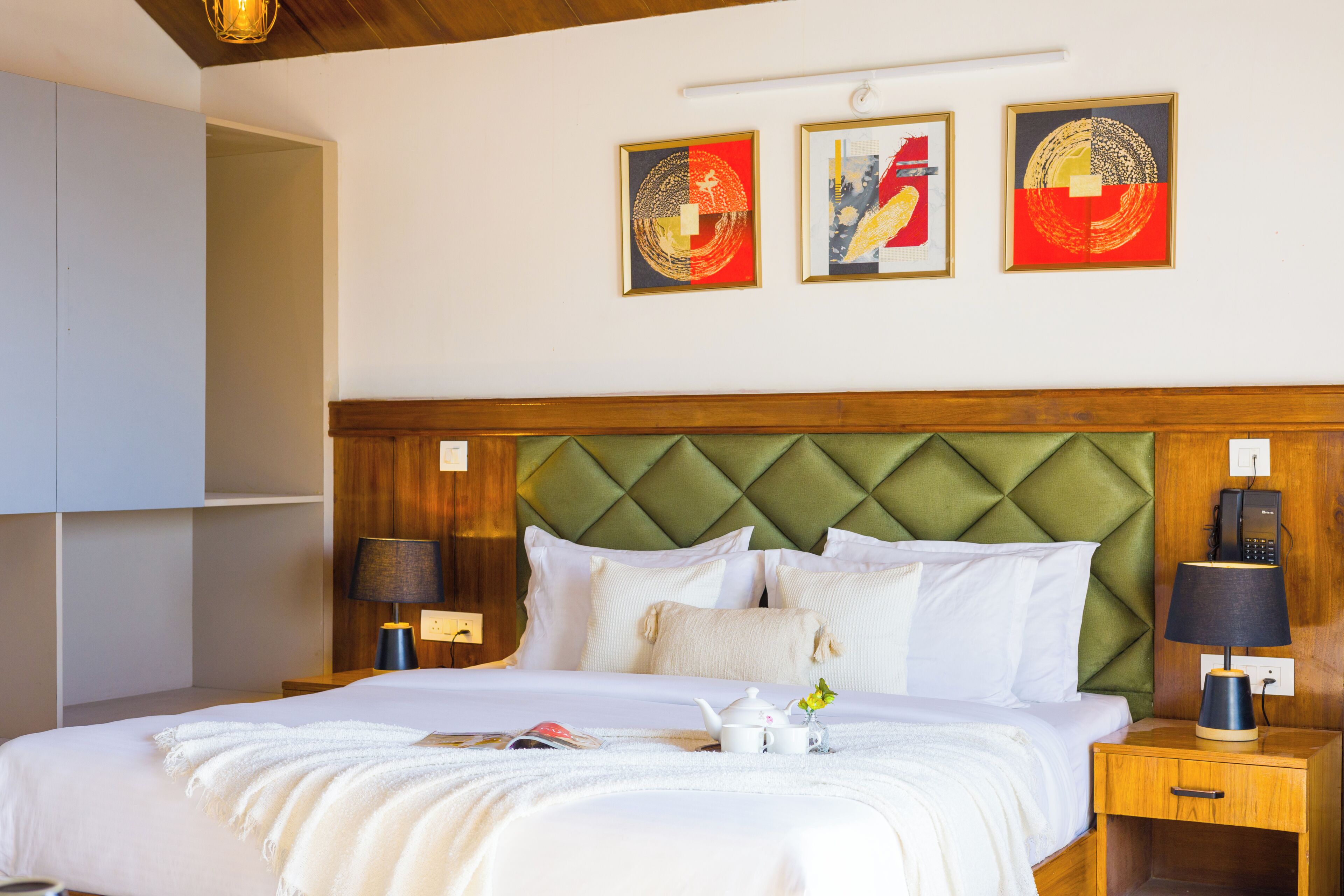 Una habitación de hotel con cama, lámparas de noche, cabecero de madera y una obra de arte en la pared.