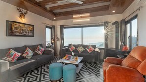 A modern living room with a sofa, ottomans, a coffee table, and a view of the outdoors. - Alaya Stays Evara Serene 4BHK Villa (Mussoorie)