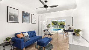 Ein modernes Wohnzimmer mit einem blauen Sofa, einem Deckenventilator und Blick auf einen Swimmingpool.