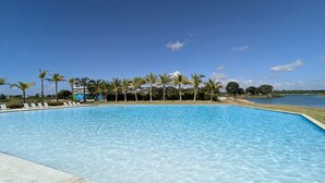 Piscina azul cristalina con sillas de descanso y palmeras, rodeada de agua y follaje.