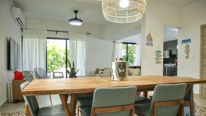 Un comedor con una mesa de madera, cuatro sillas, una lámpara colgante y una cocina al fondo.