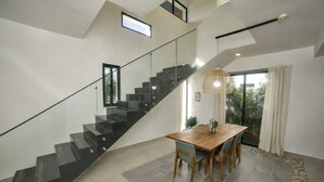 Un interior moderno con una escalera, zona de comedor y ventanas amplias.