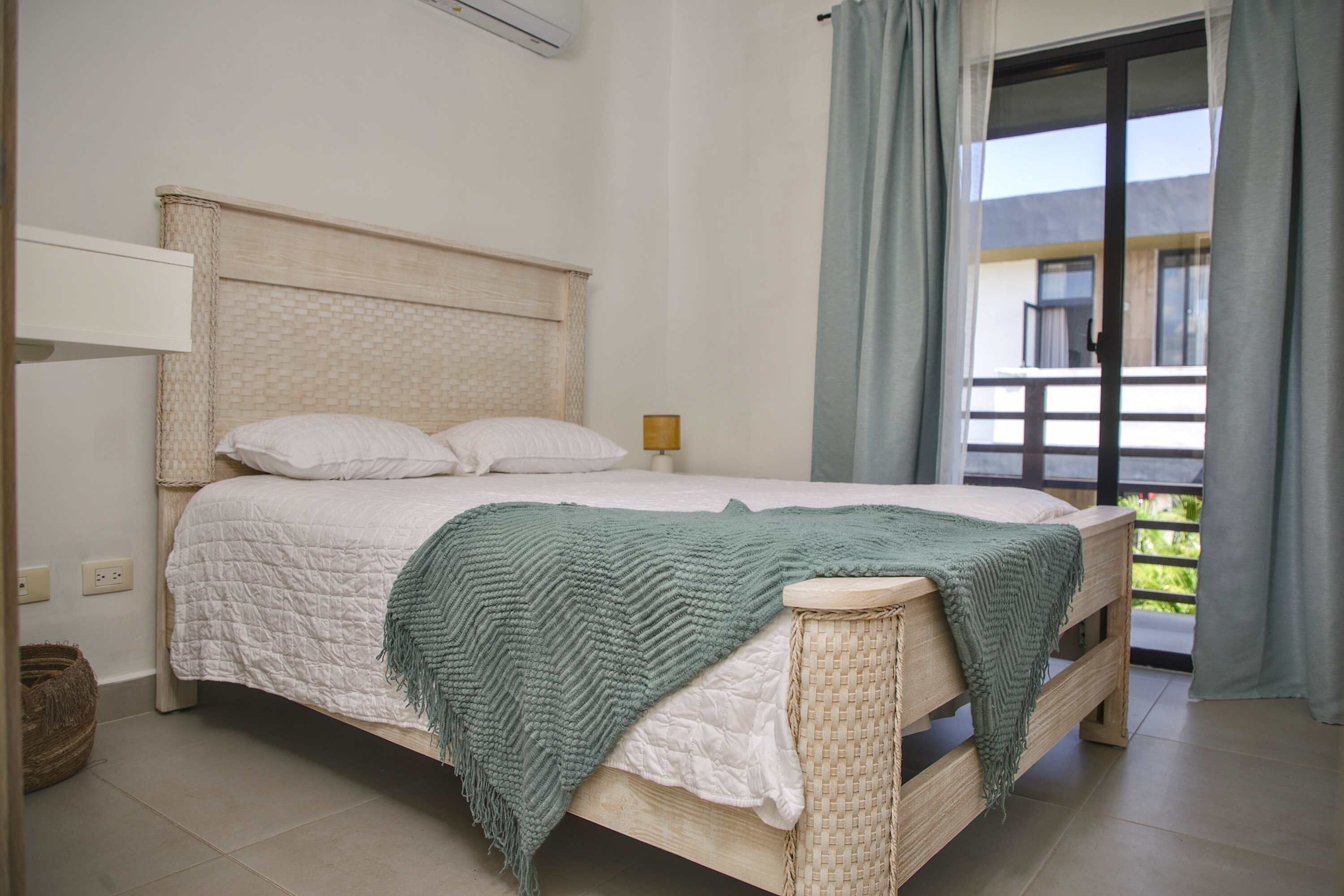 A bed with a headboard, a bedside table, and a view of a balcony.