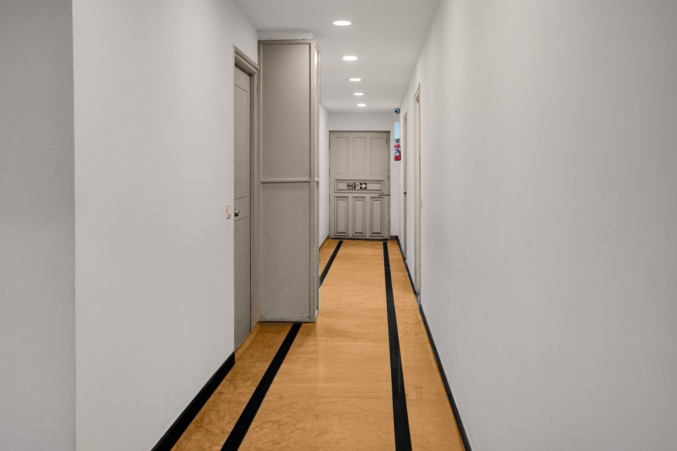 A narrow hallway with a striped carpet, white walls, and doors leading to rooms.