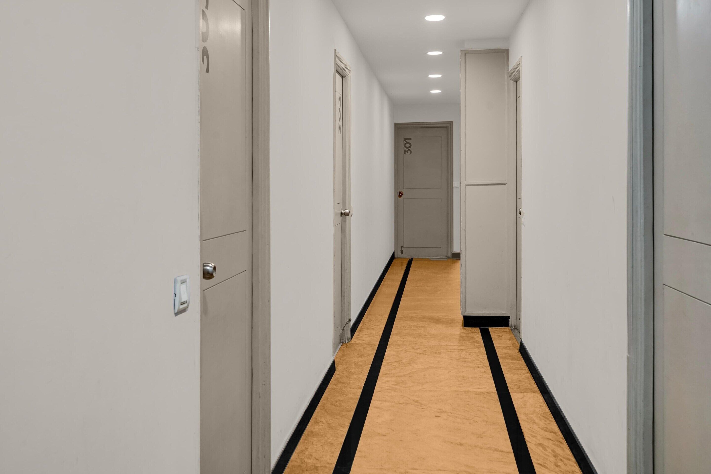 A narrow hallway with white walls, a black stripe on the floor, and doors numbered 301.