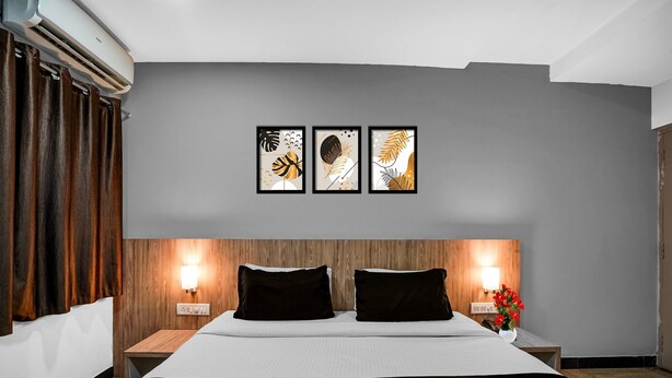 Una habitación de hotel moderna con una cama grande, cabecera de madera, dos mesitas de noche con lámparas y tres cuadros en la pared.
