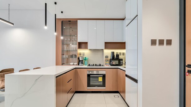 A modern kitchen with white cabinets, a built-in oven, and a marble countertop. - Free Housekeeping Visits During Your Stay - Stayshort - Fresh 2 Bedroom Apartment in JVC That Sleeps 5 (Dubai)
