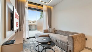 A modern living room with a sofa, a coffee table, a TV, and a view of buildings outside. - Free Housekeeping Visits During Your Stay - Stayshort - Fresh 2 Bedroom Apartment in JVC That Sleeps 5 (Dubai)