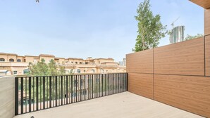 A balcony with a wooden floor, a black railing, and a view of buildings in the background. - Free Housekeeping Visits During Your Stay - Stayshort - Fresh 2 Bedroom Apartment in JVC That Sleeps 5 (Dubai)