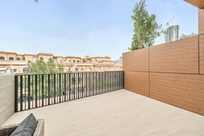 Ein Balkon mit Holzboden, schwarzem Geländer und Blick auf Gebäude im Hintergrund.