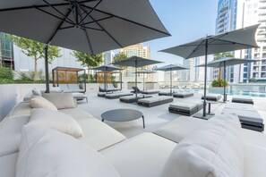 A rooftop lounge area with outdoor seating, umbrellas, and a pool view. - Free Housekeeping Visits During Your Stay - Stayshort - Modern 3 Bedroom in Business Bay That Sleeps 6 (Dubai)